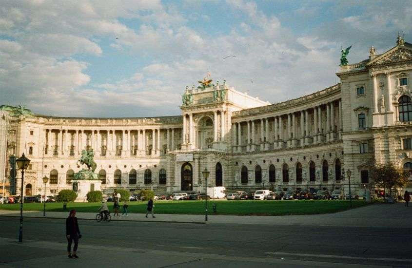 durante o dia, pessoas caminhando em frente a grande palácio, um dos pontos turísticos de viena