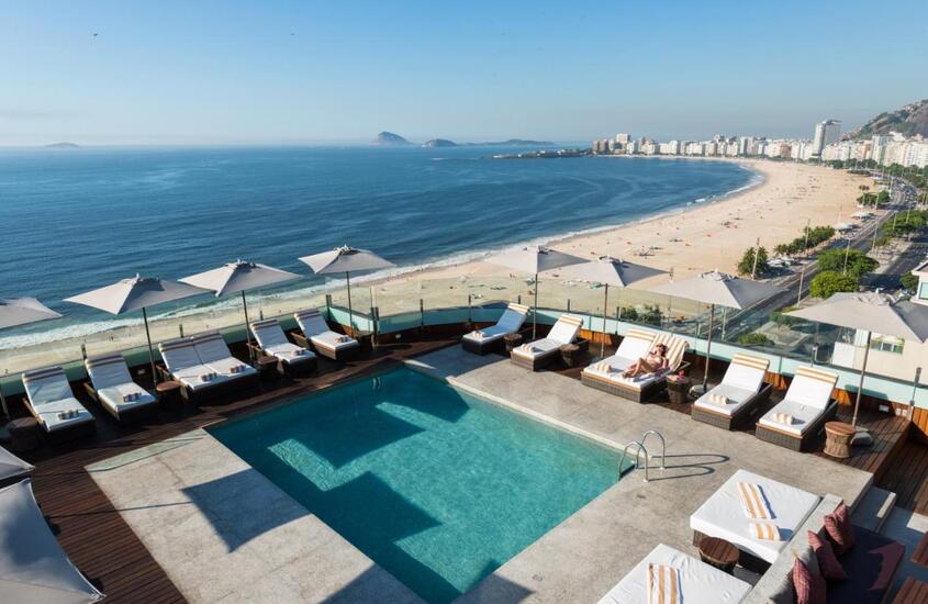durante o dia, vista aérea de espreguiçadeiras ao redor de piscina em cobertura de hotel com vista para o mar