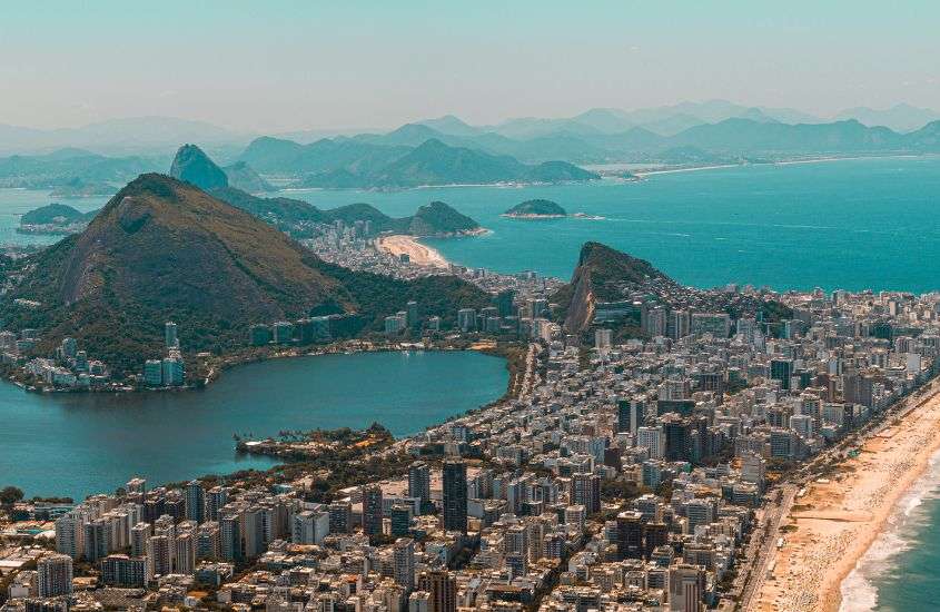 durante o dia, vista aérea de prédios, mar e morros visto de alto vidigal brasil, lugar para o reveillon rio de janeiro