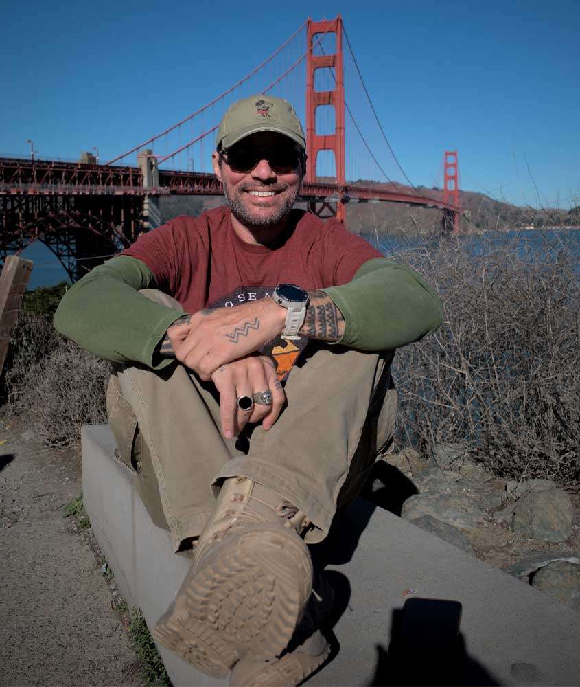 Em um dia de sol, Vagner Alcantelado, criador do blog melhores momentos da vida, com Golden Gate Bridge atrás com árvores ao redor
