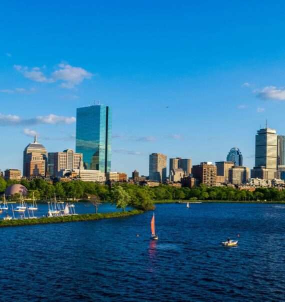 durante o dia, vista aérea de barcos em mar e, ao fundo, prédios e arranha-céus em Boston EUA