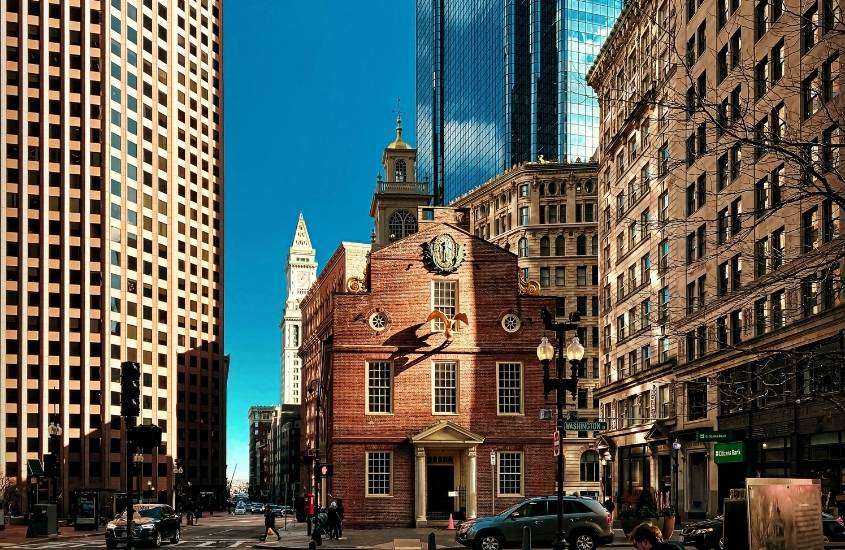 durante o dia, prédio com tijolos vermelhos e arranha céus em rua de Boston EUA