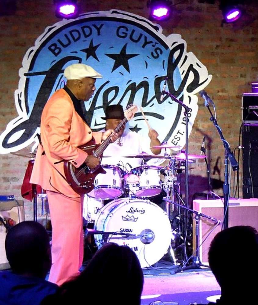 músico com boina branca e terno laranja tocando guitarra vermelha em palco de um clube de jazz em chicago eua