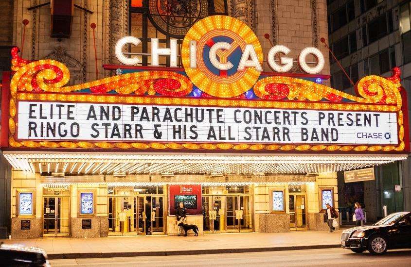 durante a noite, carros e pessoas passando em frente a fachada iluminada de teatro em chicago