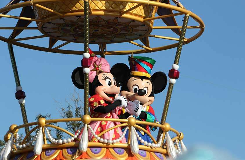 durante o dia, casal fantasiado com roupas dos personagens Minnie e Mouse, passeiam de balão em parque da Disney