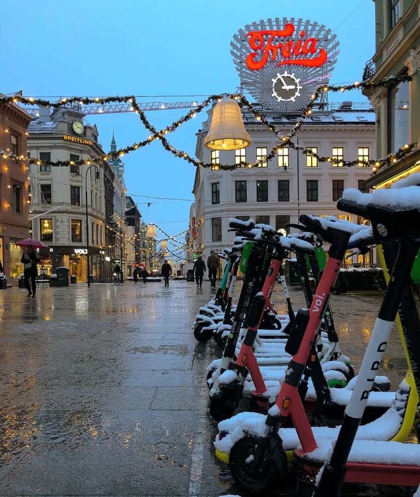 durante anoitecer, diversos patinetes cobertos de neve em rua decorada com pisca-pisca de natal