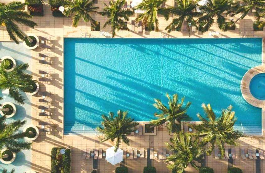 durante dia ensolarado, vista aérea de espreguiçadeiras e árvores ao redor de piscina de um hotel em miami