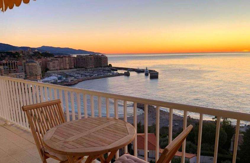 durante entardecer, cadeiras e mesa de madeira em varanda de um dos melhores hotéis em mônaco com vista para o mar