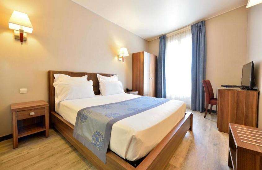 mesa de cabeceira de madeira, cama de casal e guarda-roupa em suíte de um dos hotéis baratos em Mônaco