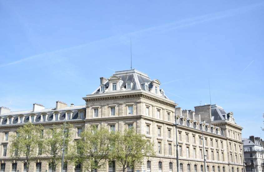 durante o dia, árvores em frente a grande construção branca com telhado cinza em Le Marais, um dos melhores bairros de paris para se hospedar