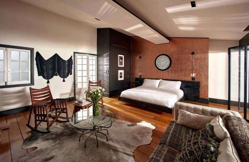 cadeiras de madeira, mesa de vidro redonda, sofá e cama de casal em suíte de um hotel na cidade do méxico