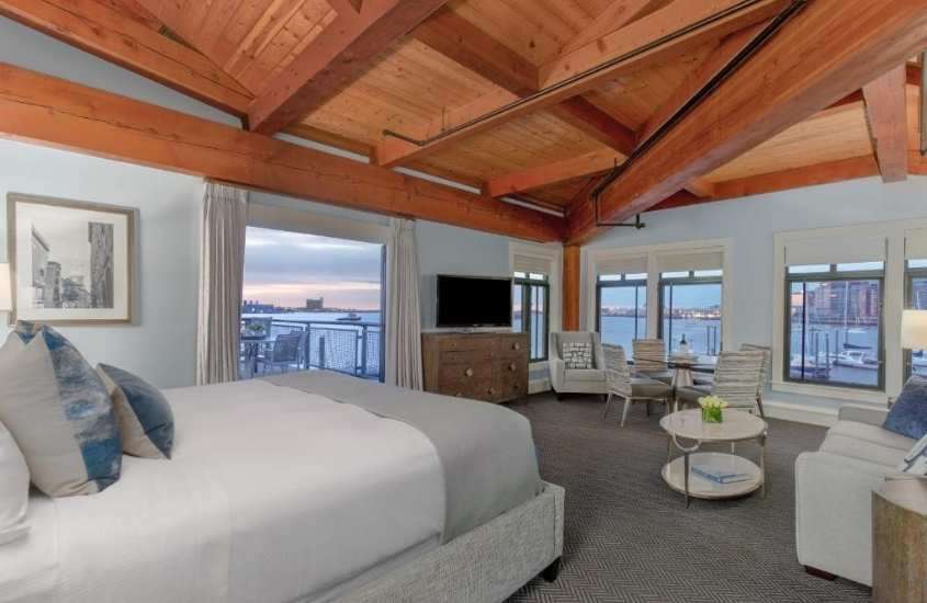 durante o dia, cama de casal, sofá, mesa, cadeiras e televisão em suíte de um dos hotéis em boston com vista para o mar