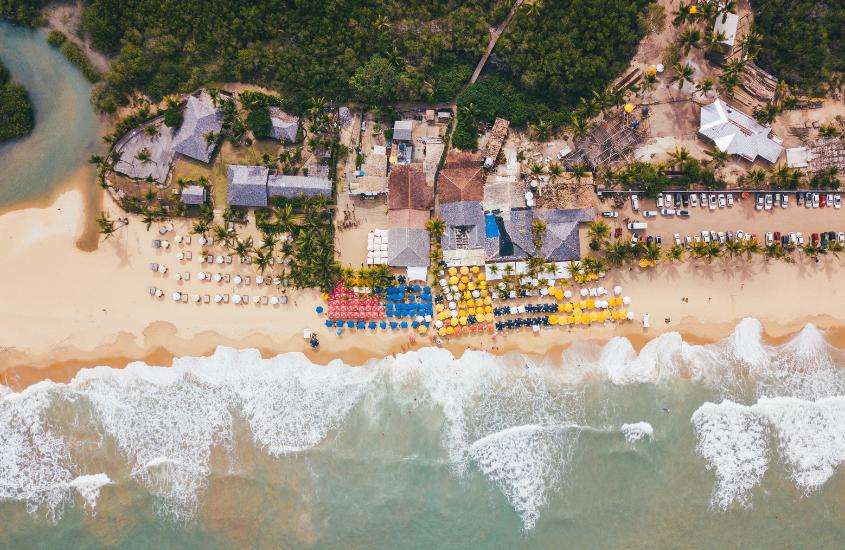 durante o dia, vista aérea de guarda-sóis coloridos em areia de praia de taperapuan, lugar para passar o Réveillon Porto Seguro 2023