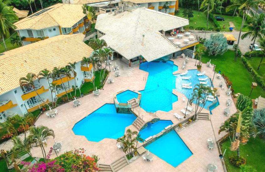 durante o dia, vista aérea de espreguiçadeiras brancas ao redor de piscinas em área de lazer ao ar livre de hotel em porto seguro