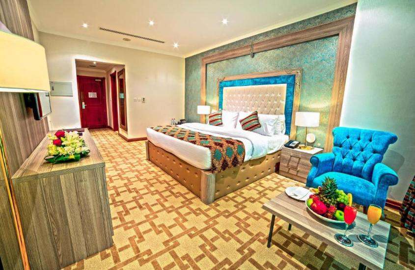 poltrona azul, taças e frutas em cima de mesa de madeira e cama de casal em suíte de um dos melhores hotéis em doha catar