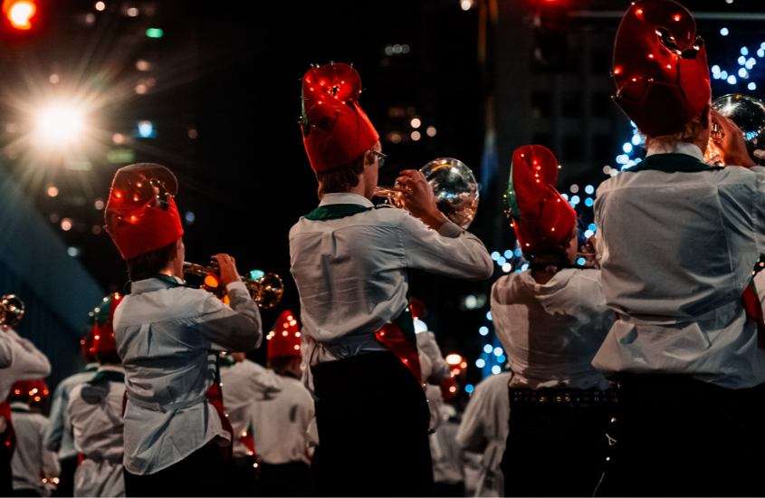 pessoas vestidas de blusa branca e chapéu vermelho, se apresentam em desfile de natal