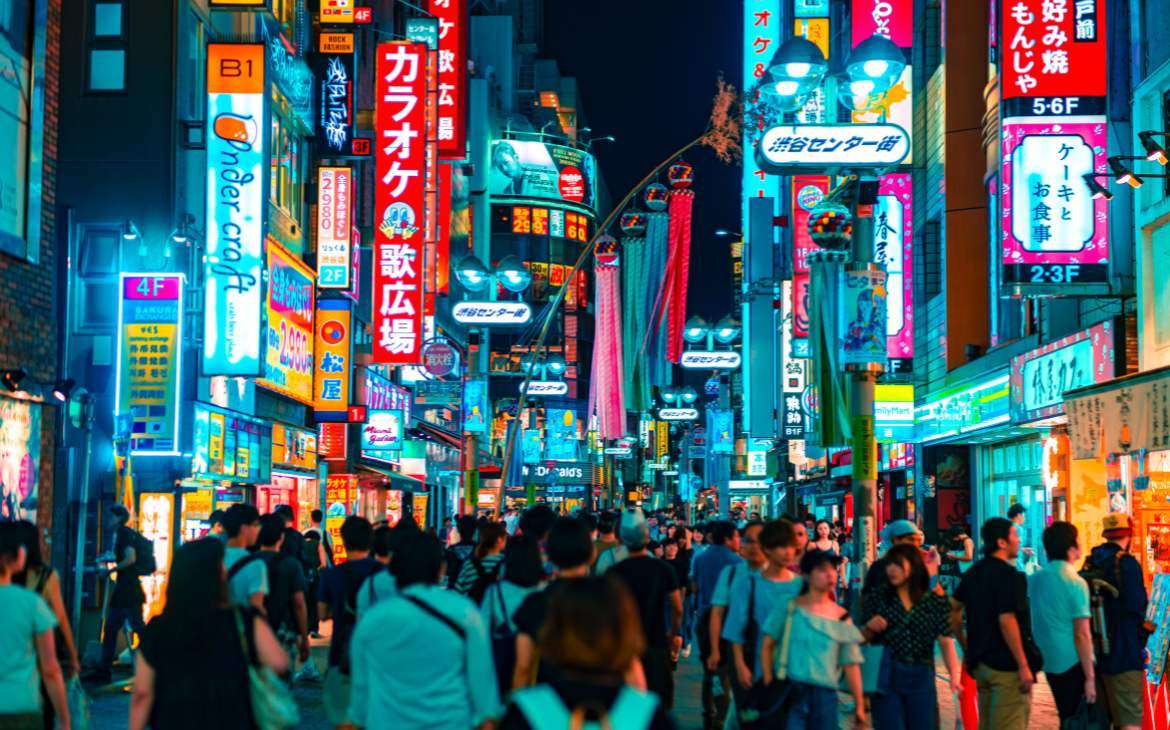 durante a noite, pessoas caminhando em rua cercada de letreiros iluminados em ruas de Tokyo Japão