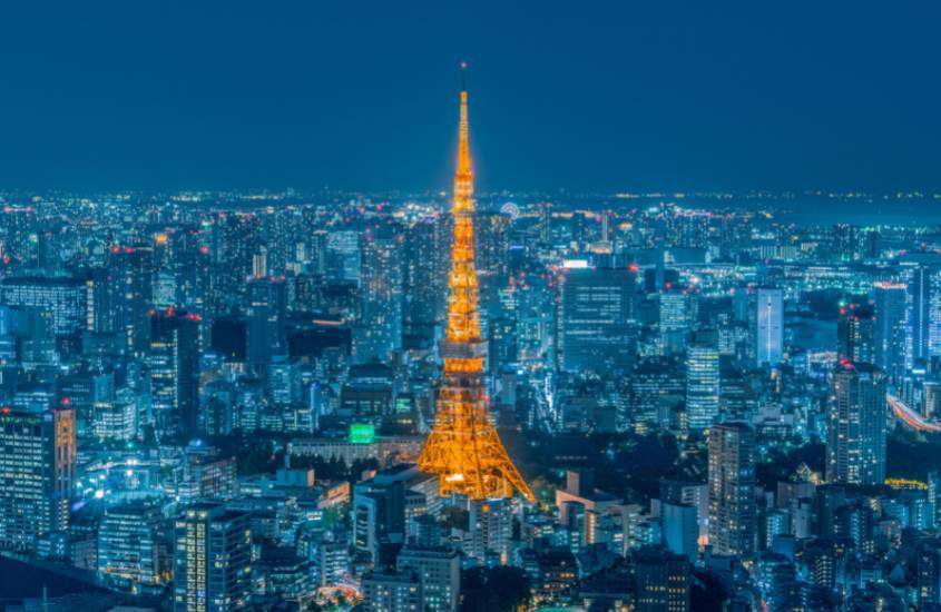 durante a noite, vista aérea de prédios iluminados em azul ao redor de torre iluminada com luz laranja em Tokyo Japão