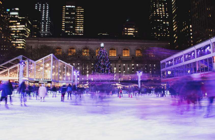 durante a noite, pessoas patindo em pista de patinação de gelo, decorada com grande árvore de natal