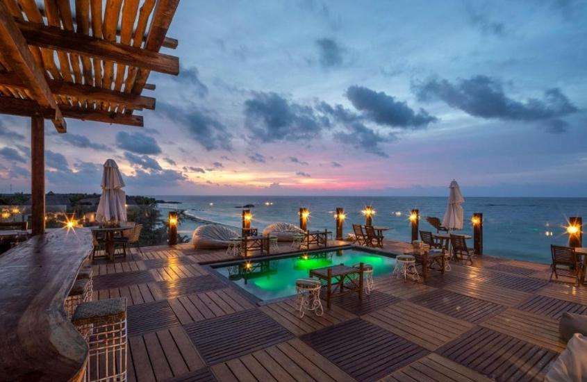 durante o dia, piscina, cadeiras e mesas em deck de madeira com vista para o mar em um dos melhores hotéis em tulum