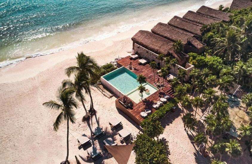 durante o dia, vista aérea de espreguiçadeiras e piscina em deck de um dos hotéis em Tulum beira mar