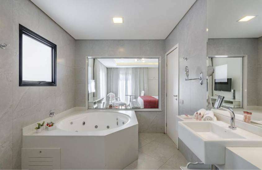 banheira de hidromassagem e pia de mármore, em banheiro com ampla janela com vista para cama de casal em quarto de hotel