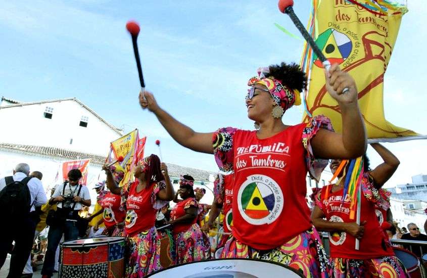 durante o dia, mulher com blusa vermelha, tocando tambor em bloco de rua do carnaval em salvador