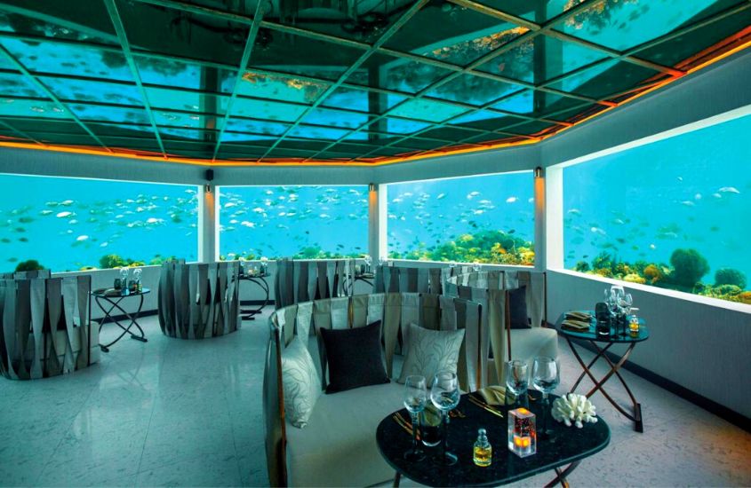 cadeiras e mesas em salão de hotel submarino nas maldivas com vista para peixes no mar