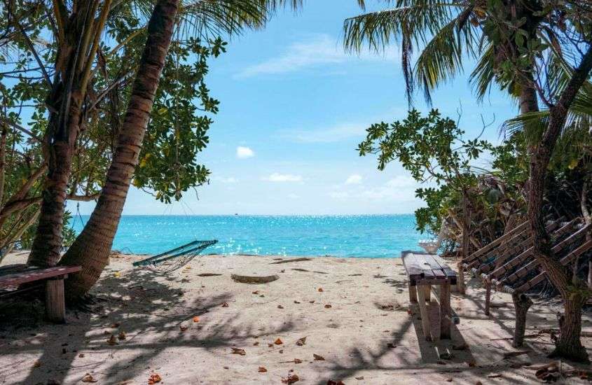 durante o dia, bancos de madeira e rede de descanso em trecho de praia privativa de um hotel nas ilhas maldivas