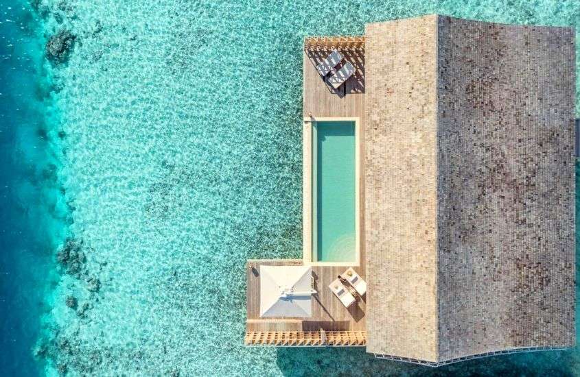 durante o dia, vista aérea de guarda-sol, espreguiçadeiras e piscina em varanda de bangalô sobre a água