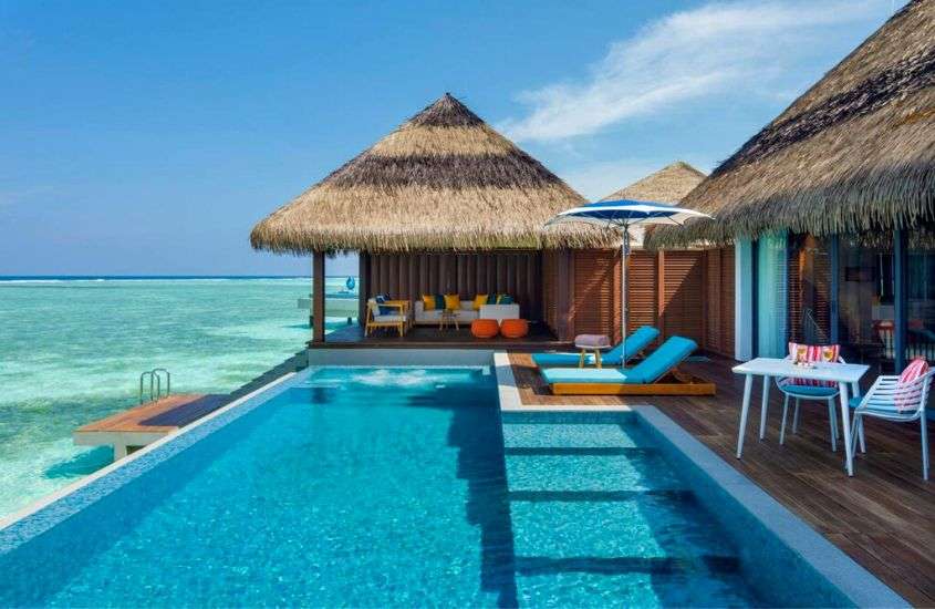 durante o dia, espreguiçadeiras, guarda-sol, cadeiras, mesas e piscina ao ar livre em varanda de hotel nas maldivas com vista para o mar