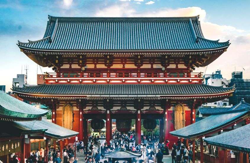 durante o dia, pessoas caminhando em frente a templo vermelho, com telhado marrom em asakusa, um lugar onde se hospedar em tokyo