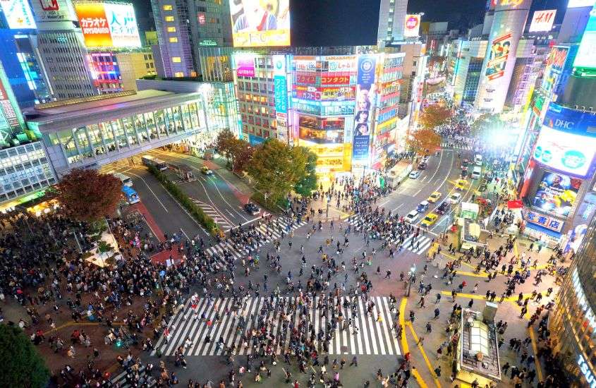 durante a noite, vista aérea de pessoas atravessando maior cruzamento do mundo, em shibuya, um lugar onde ficar em tokyo