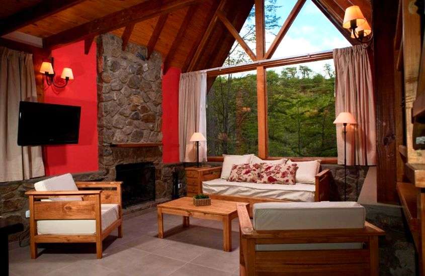 durante o dia, poltronas, mesa, tv e sofá em sala de estar de um dos hotéis em ushuaia com vista para natureza