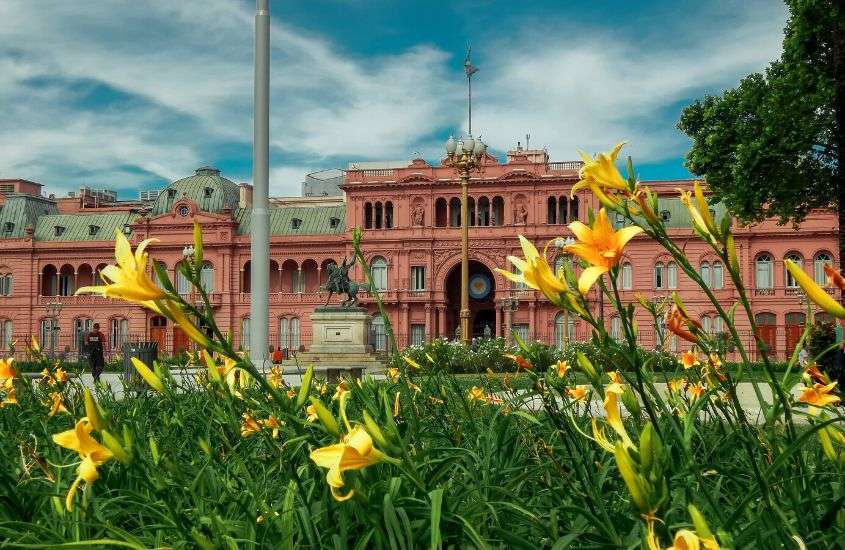 durante o dia, flores amarelas em jardim em frente a grande prédio rosa, um dos principais pontos turísticos da argentina