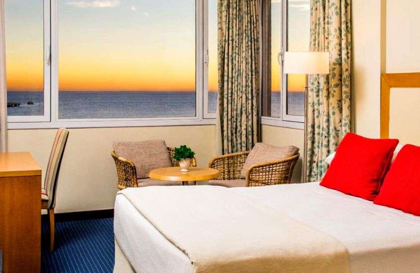 durante entardecer, cama de casal e poltronas em suíte de hotel com vista para o litoral da argentina