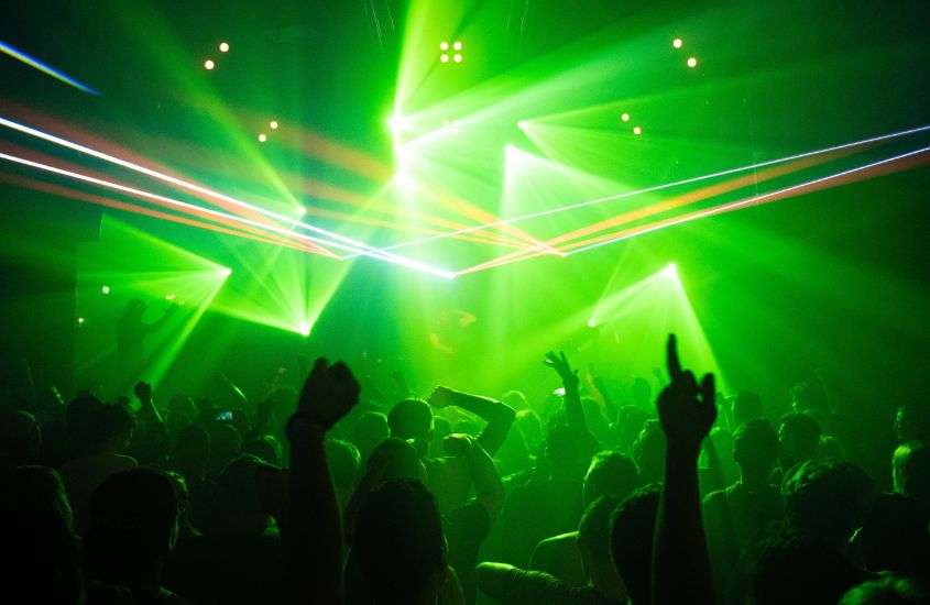 silhueta de pessoas dançando iluminadas por luzes verdes em balada, um dos em lugares para passar réveillon em balneário camboriú