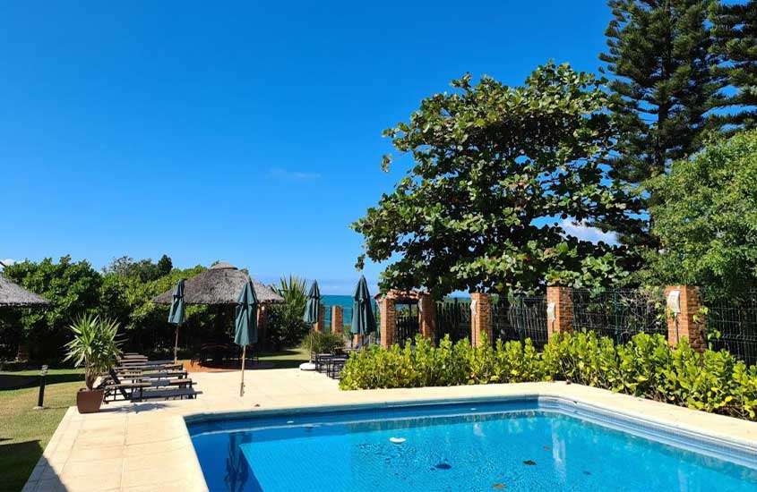durante um dia ensolarado, espreguiçadeiras em frente a piscina em área de lazer ao ar livre de casa rodeada por árvores e com vista para o mar