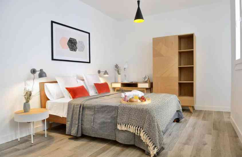 cama de casal, mesa de escritório e armário de madeira em suíte de hotel