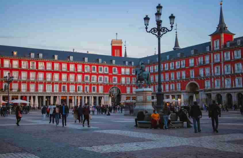 durante o dia, pessoas caminhando em frente a palácio vermelho com telhado cinza em puerta del sol, um lugar onde ficar em Madri