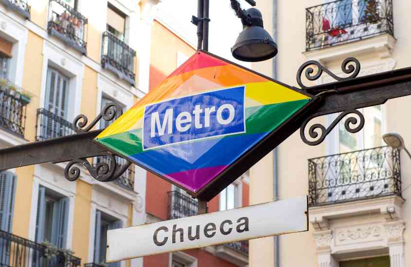 durante o dia, frase 'metro chueca' escrita em placa colorida, pendurada em rua de chueca, lugar onde ficar em Madri