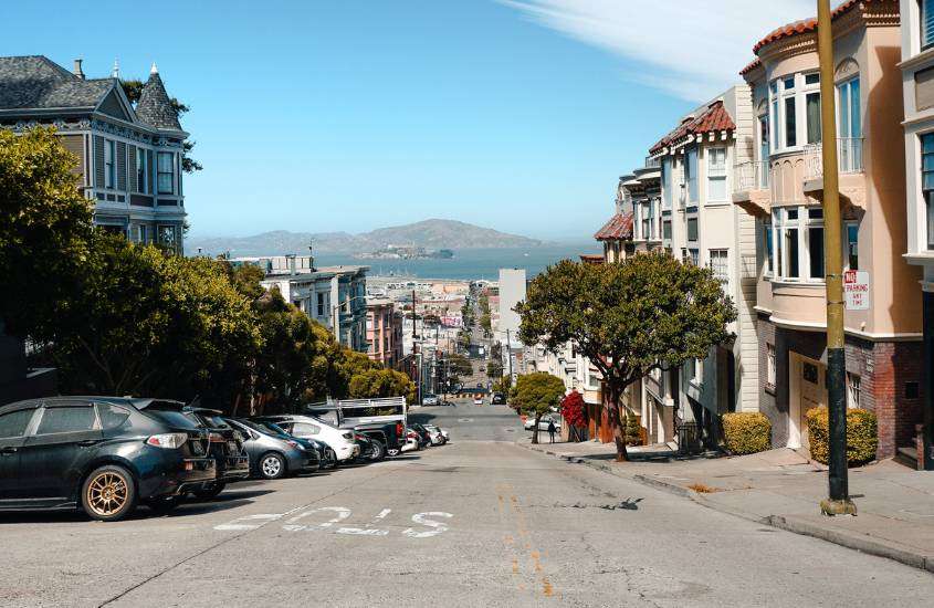 durante o dia, carros estacionados em frente a casas coloridas em rua inclinada com vista para o mar
