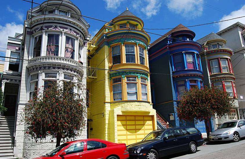 durante o dia, diversos carros estacionados em rua cheia de casas coloridas em um dos bairros de San Francisco