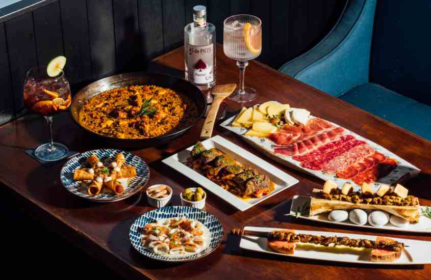 diversas tapas (aperitivos) da cultura espanhola e taças de drinks em cima de mesa de madeira