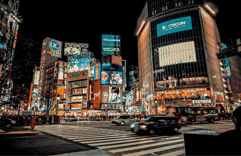 durante a noite, carros passando em avenida de tokyo enquanto pessoas esperam para atravessar na faixa de pedestres