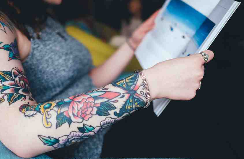 braço de pessoa branca com diversas tatuagens de flores coloridas