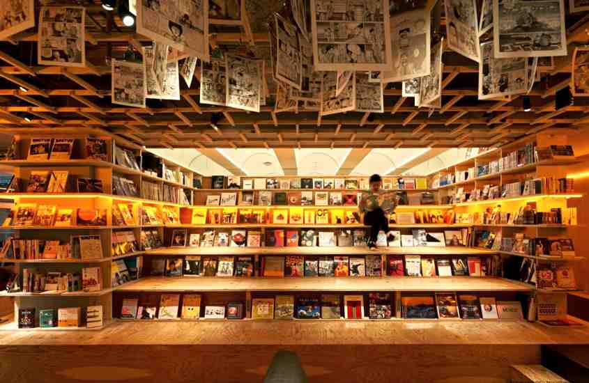 páginas de livros pendurados em teto e diversas prateleiras com livros em salão de hotel no japão