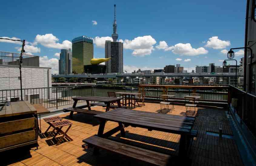bancos, mesas e cadeiras de madeira em varanda de hotel no japão com vista para rio e prédios