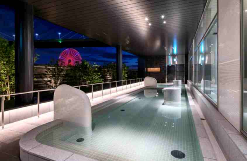durante a noite, piscina retangular em varanda coberta de hotel com vista para roda-gigante iluminada por luz vermelha