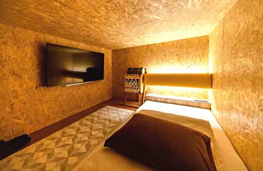 TV preta, tapete e colchão de solteiro em acomodação de hotel cápsula com paredes de madeira